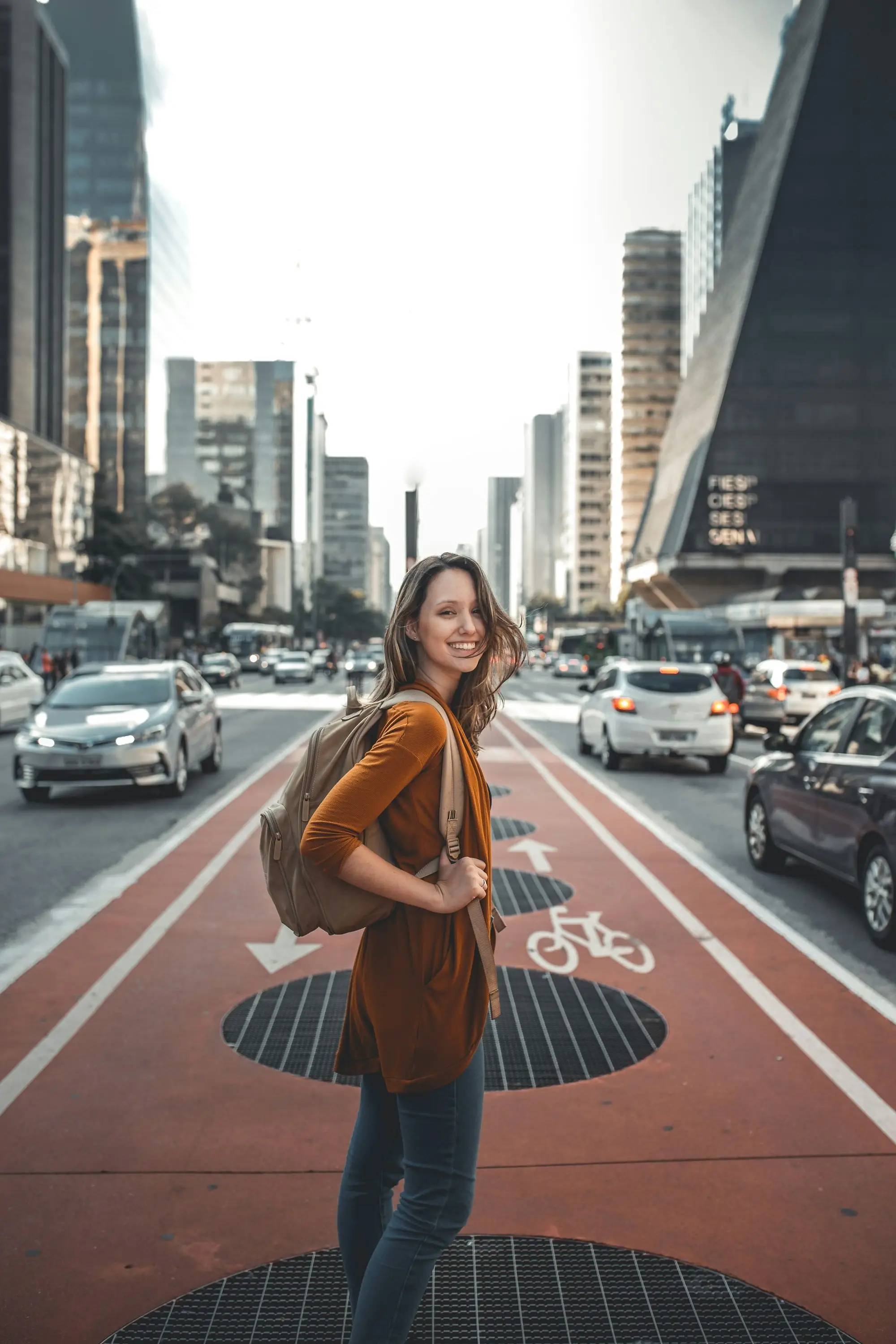 A smiling woman with a backpack standing on a city street